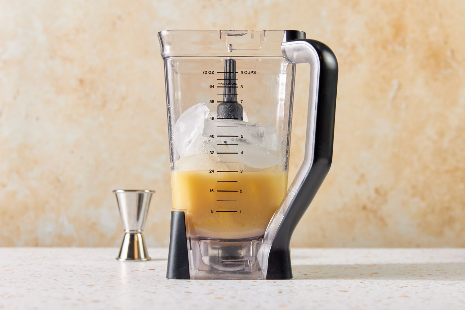 Blender With White Rum, Coconut Cream, Pineapple Juice & Fruit, and Ice Next to a Jigger for PiÃ±a Colada Recipe