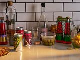 A kitchen countertop with a mix of snacks, alcoholic beverages, and non-alcoholic beverages like Ghia and Phony Negroni