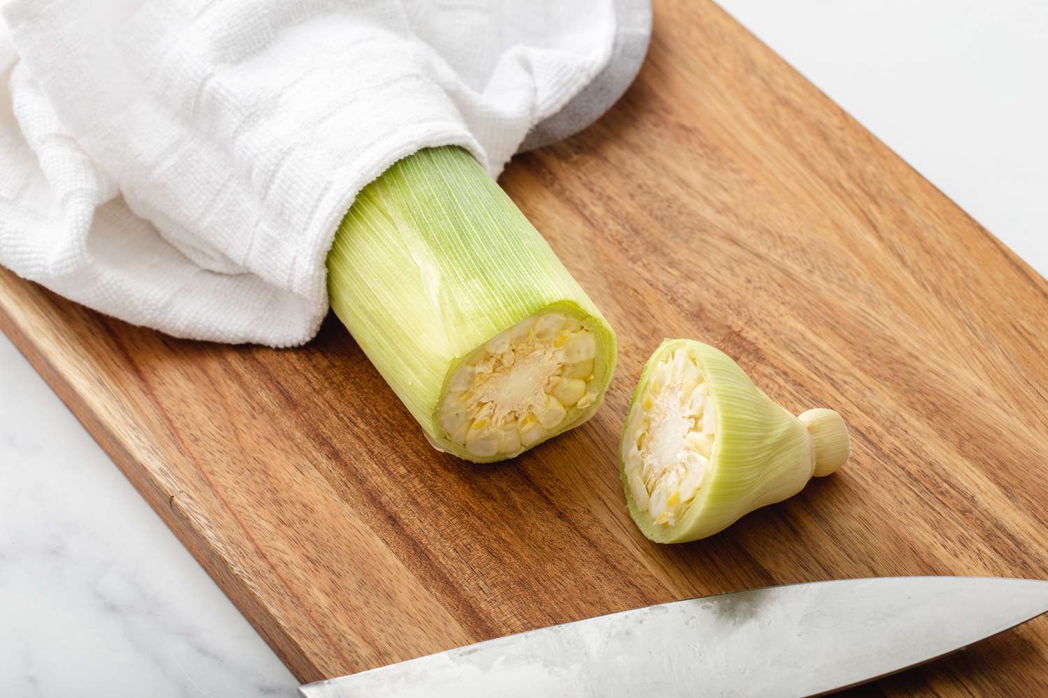 Slicing the end of the corn off on a cutting board to show how to make corn on the cob.