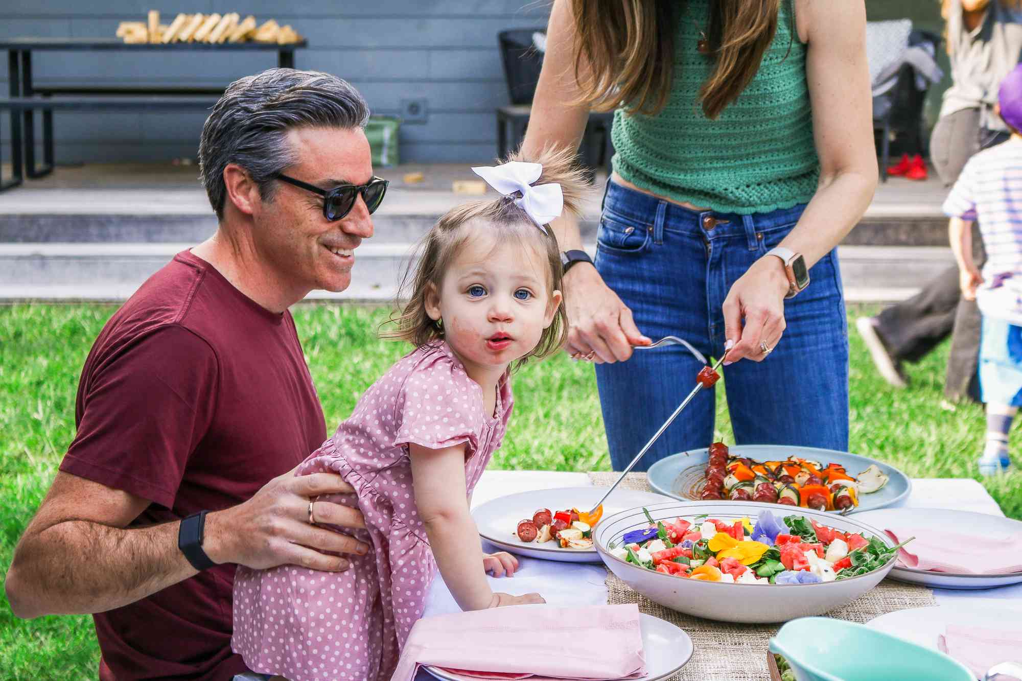 The Pfeffer family serving food at the outdoor table, a smile child with a bow in her hair looking at the camera