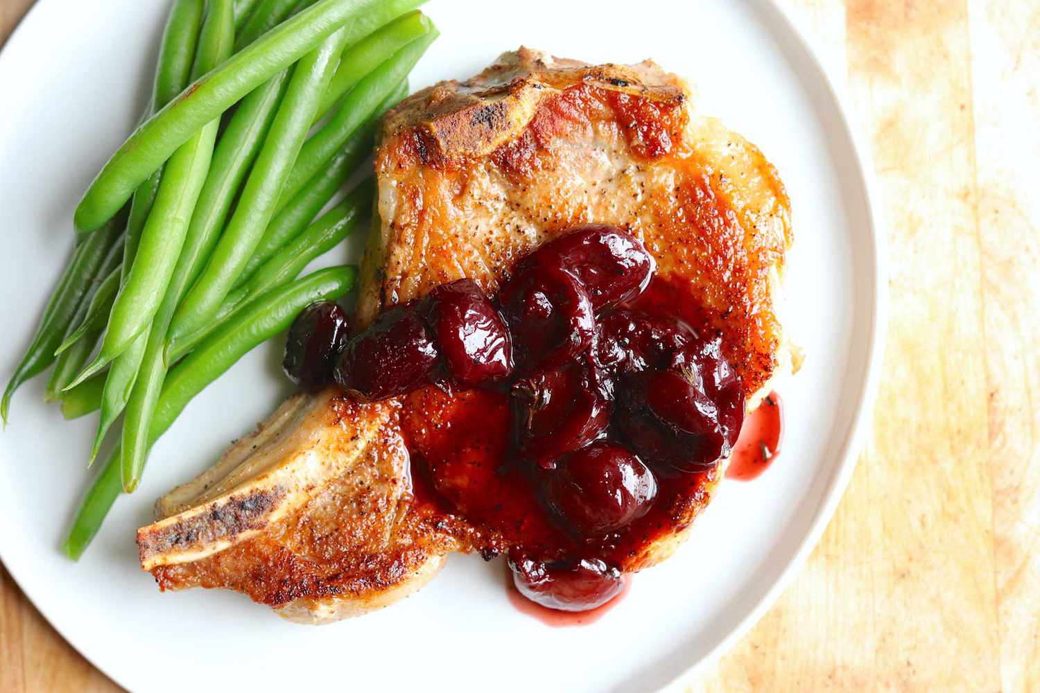 pork chops in a cherry sauce with a side of green beans on a white plate