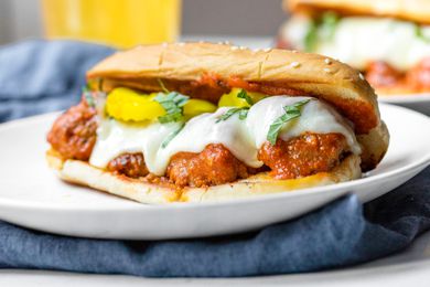 A Plate of Meatball Sub Topped with Banana Peppers and Basil, and in the Background, a Plate With Another Sub and a Glass of Beer