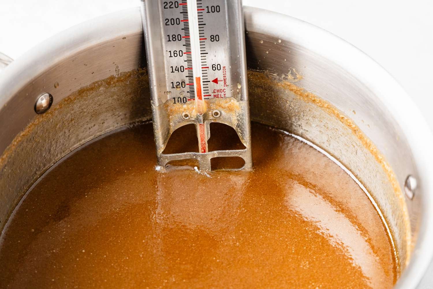 Melty penuche mixture cooling down in a pot with thermometer reading around 130F
