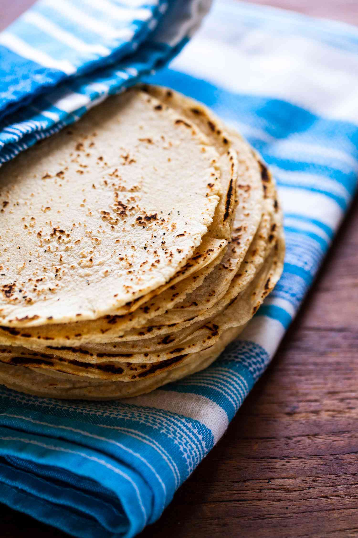 Corn tortillas stacked on a blue striped linen and being partially covered by the linen 