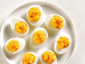 Overhead view of deviled eggs with paprika, mustard and mayonnaise on plate over white stone background.