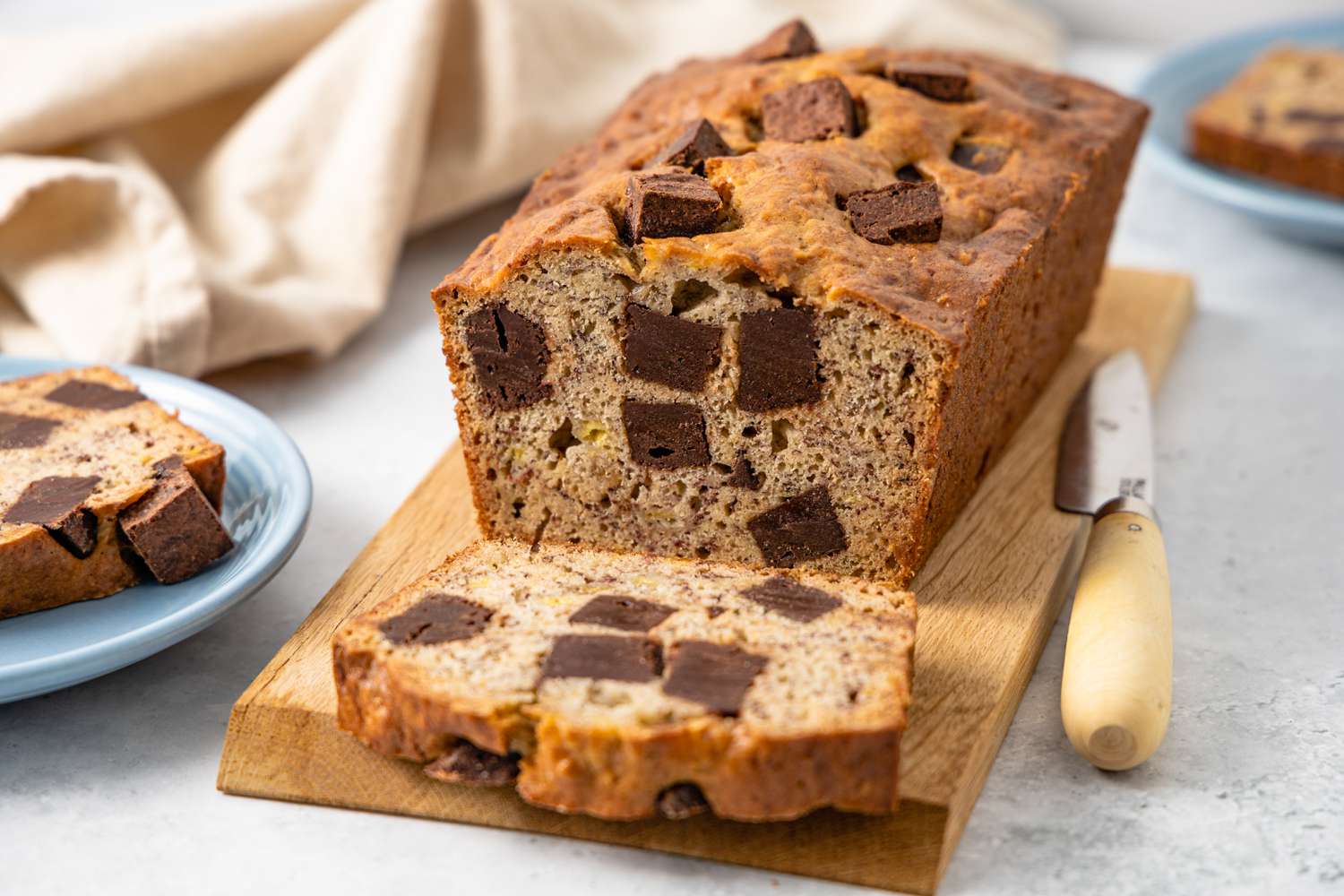 On a Wooden Board, Loaf of Brownie Banana Bread with Slices Cut Off, and Next to It, a Plate with a Slice and a Knife