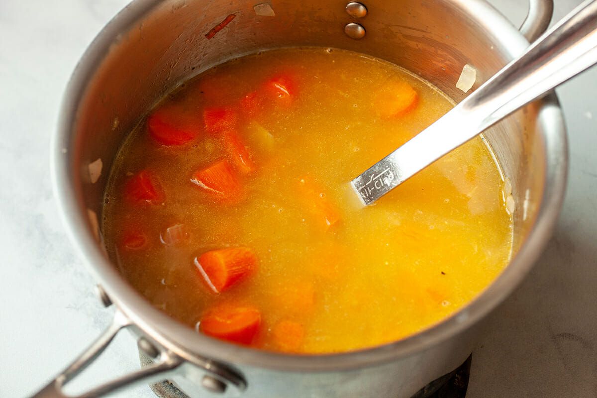 Carrots, onions, and stock cooking in a pan with a spoon 