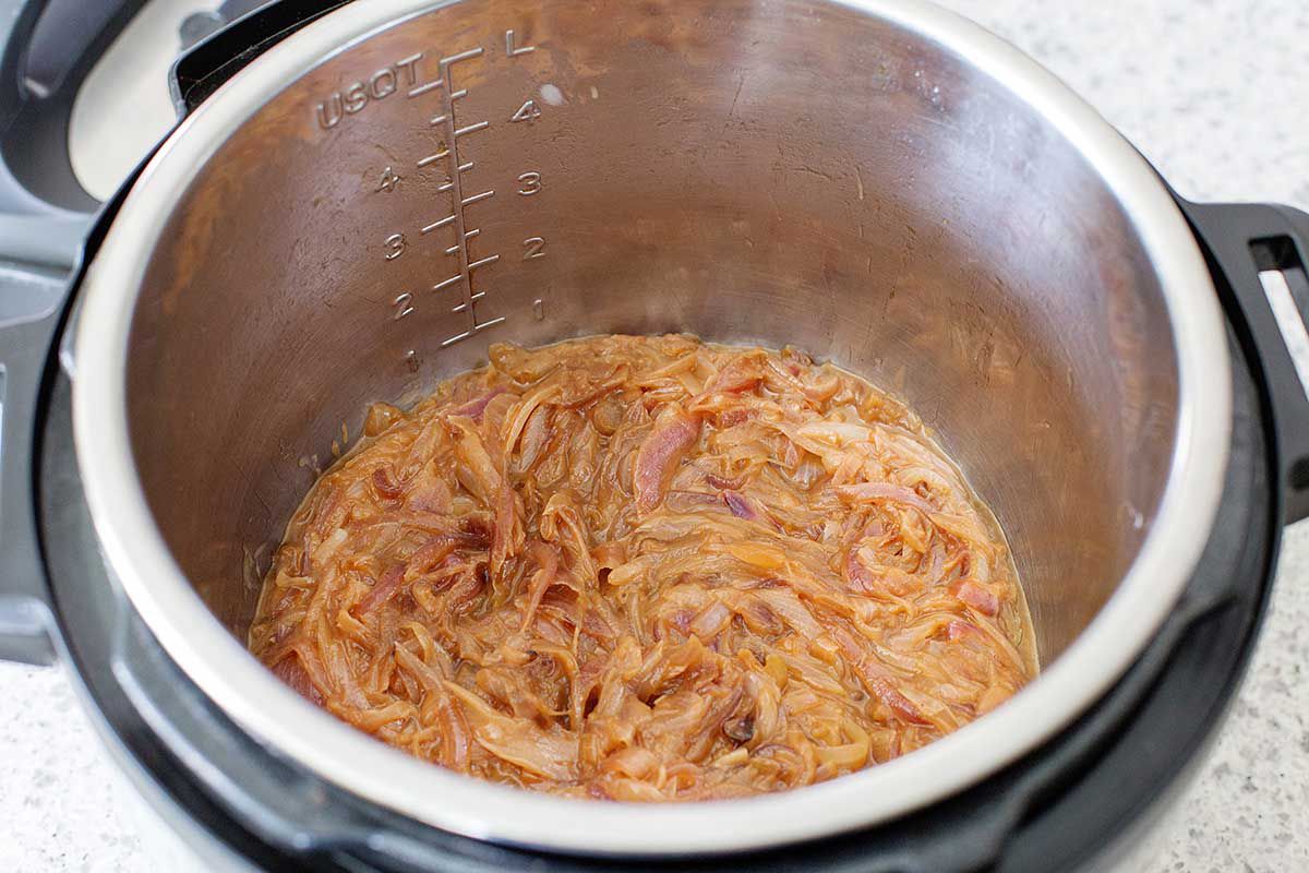 Cooked onions for the best Instant Pot French Onion Soup in the bottom of a silver instant pot bowl