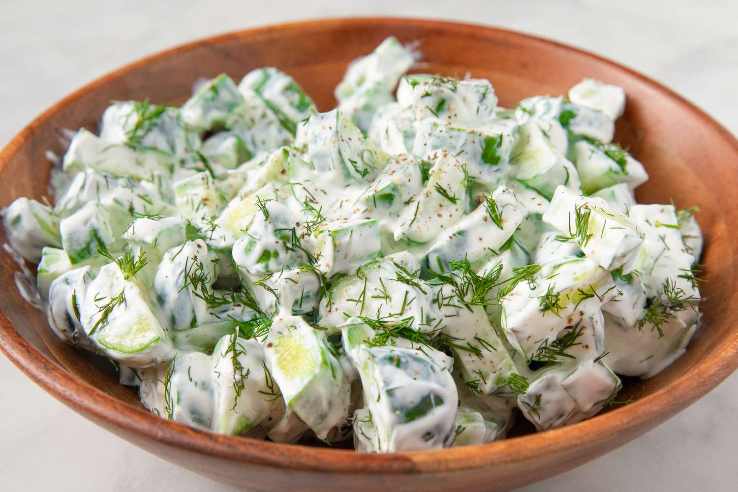 Cucumber salad in a wooden bowl, garnished with fresh dill and a creamy dressing