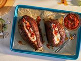 Two whole roasted eggplant on a baking sheet, topped with yogurt and chili crisp, a bowl of chili crisp alongside