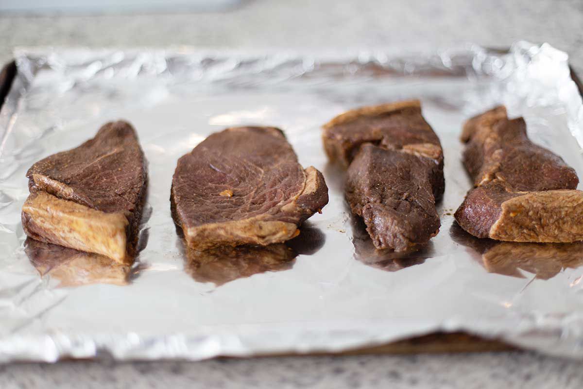 Four balsamic marinated steaks on foil on a baking sheet.
