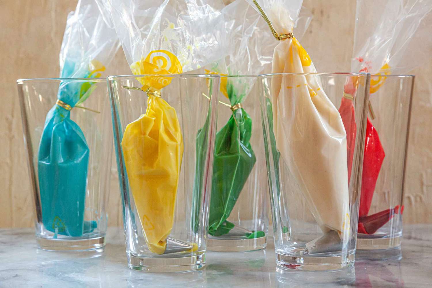 5 piping bags set in glasses and filled with various colors of royal icing.