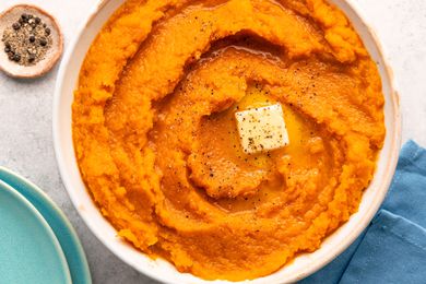 Overhead view of a white bowl of butternut squash topped with butter ad spices resting on a blue table napkin
