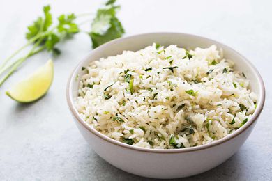 A bowl of cilantro lime rice with a cilantro and a lime wedge in the background