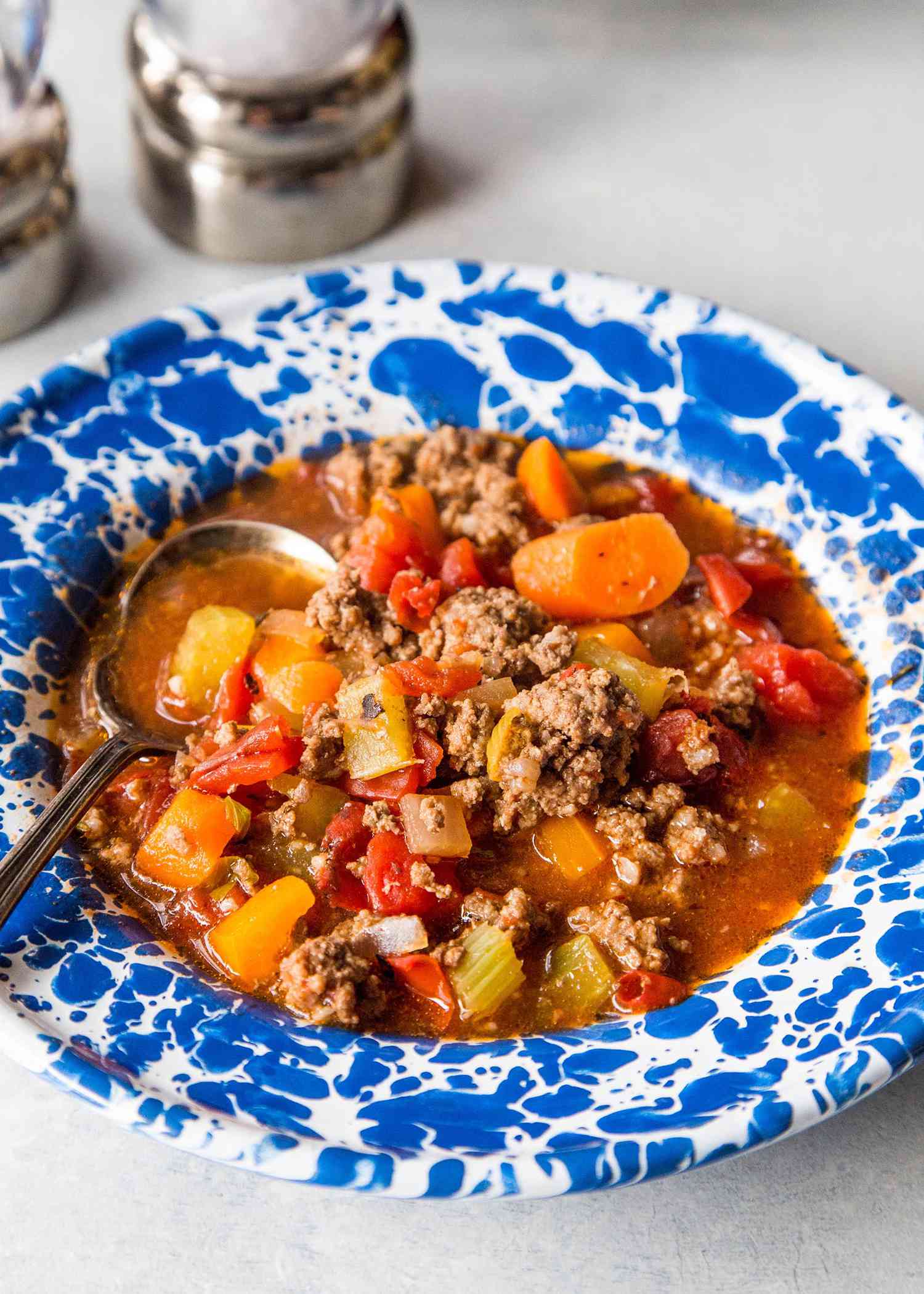 Hamburger soup with vegetables resting in a blue bowl 