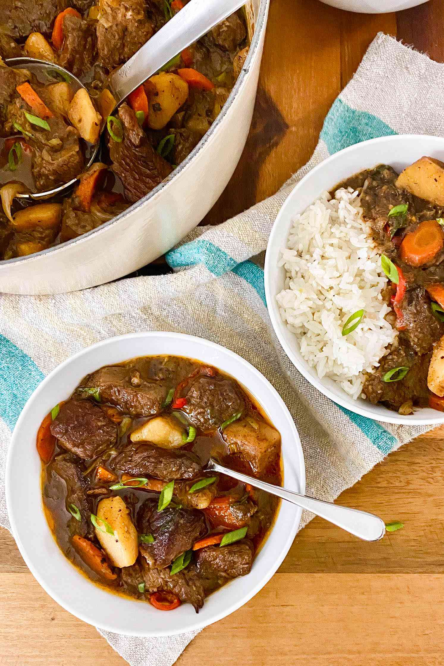 Two bowls of Jamaican beef stew on a table with a pot in of stew 