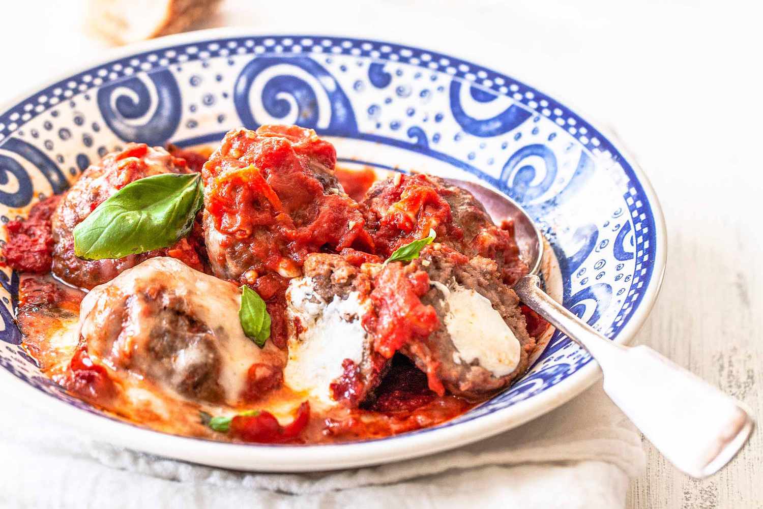 Mozzarella stuffed meatballs in a blue and white bowl with a spoon
