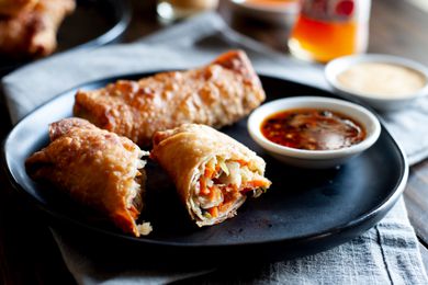 A dark plate with stacked vegetable egg rolls and dipping sauce