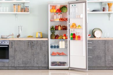 Open refrigerator in a modern kitchen, shelves filled with food and beverages