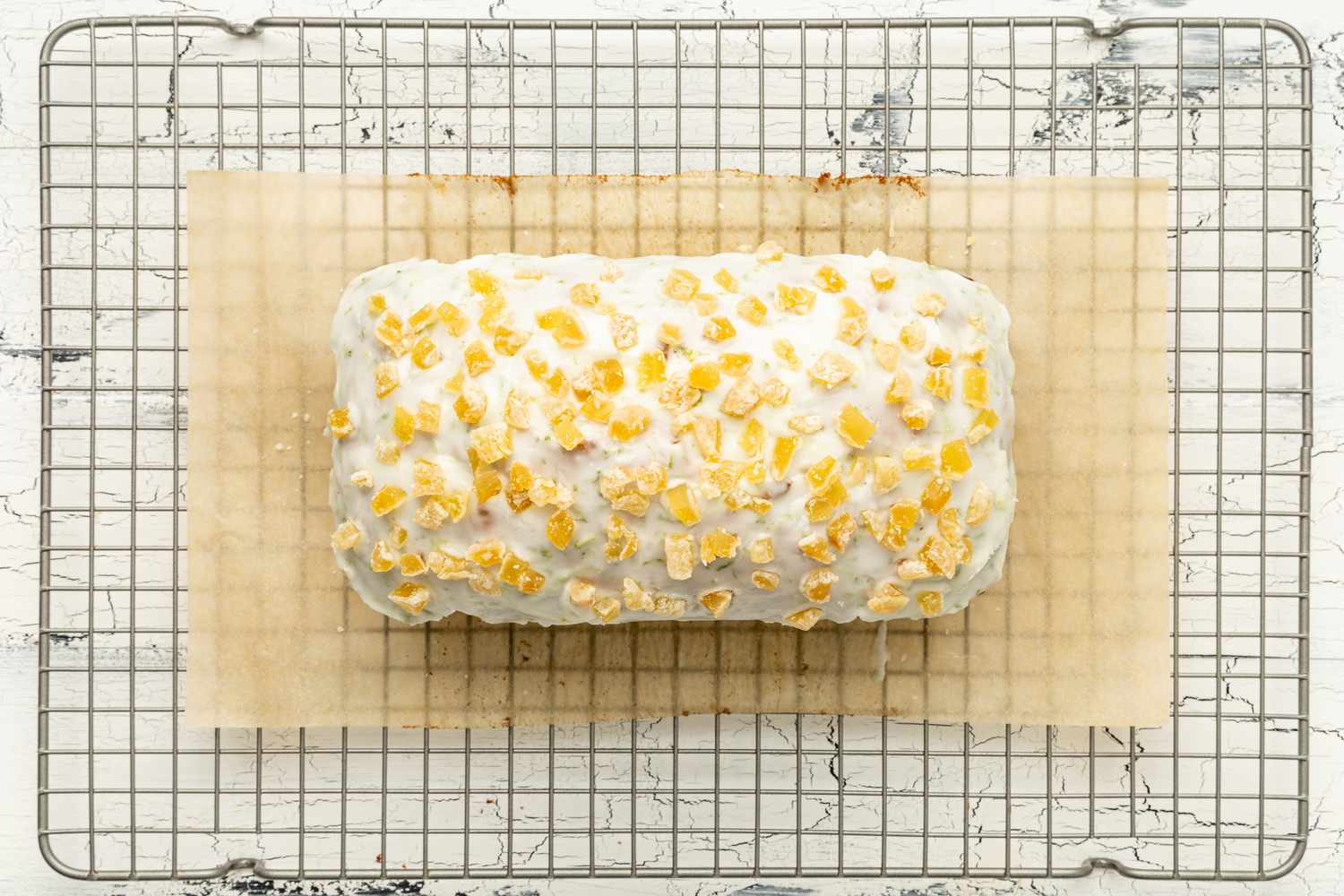 Dark and Stormy Banana Bread Topped With Glaze and Candied Ginger on a Parchment Paper Lined Cooling Rack