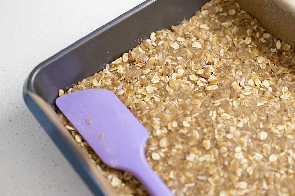 Caramel Chocolate Oatmeal Bars - purple spatula smoothing oatmeal