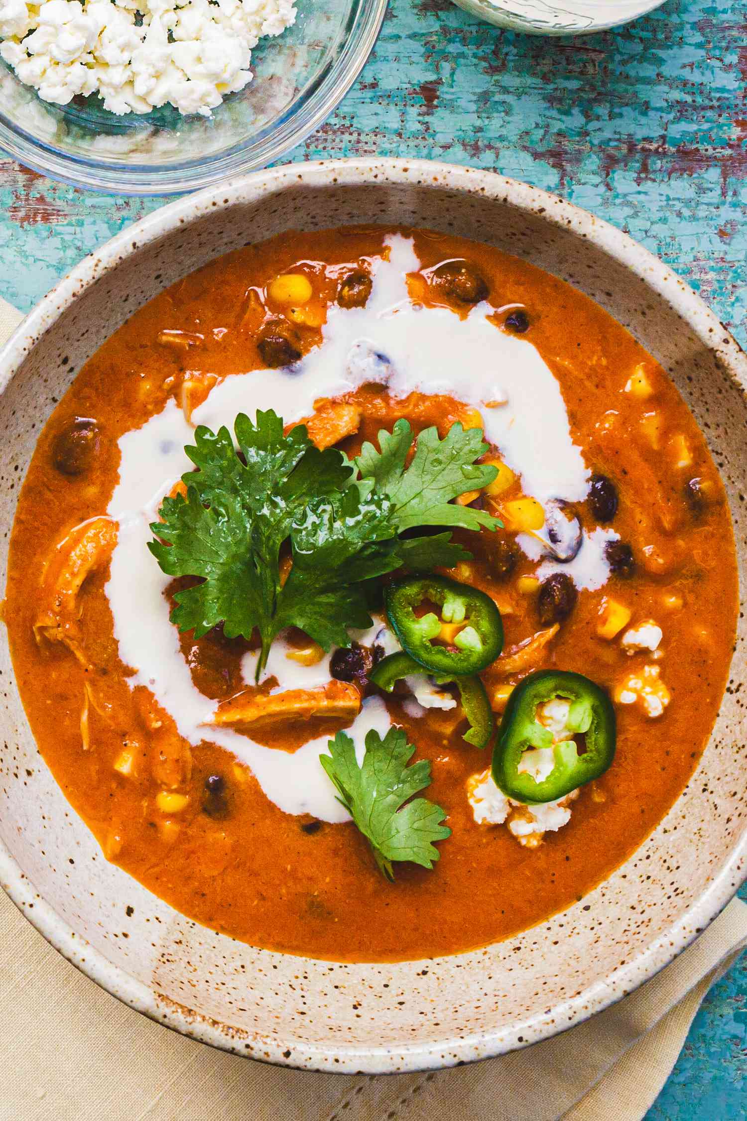 A bowl of creamy chicken enchilada soup with a sour cream swirl on top and a garnish of cilantro and sliced fresh jalapeno