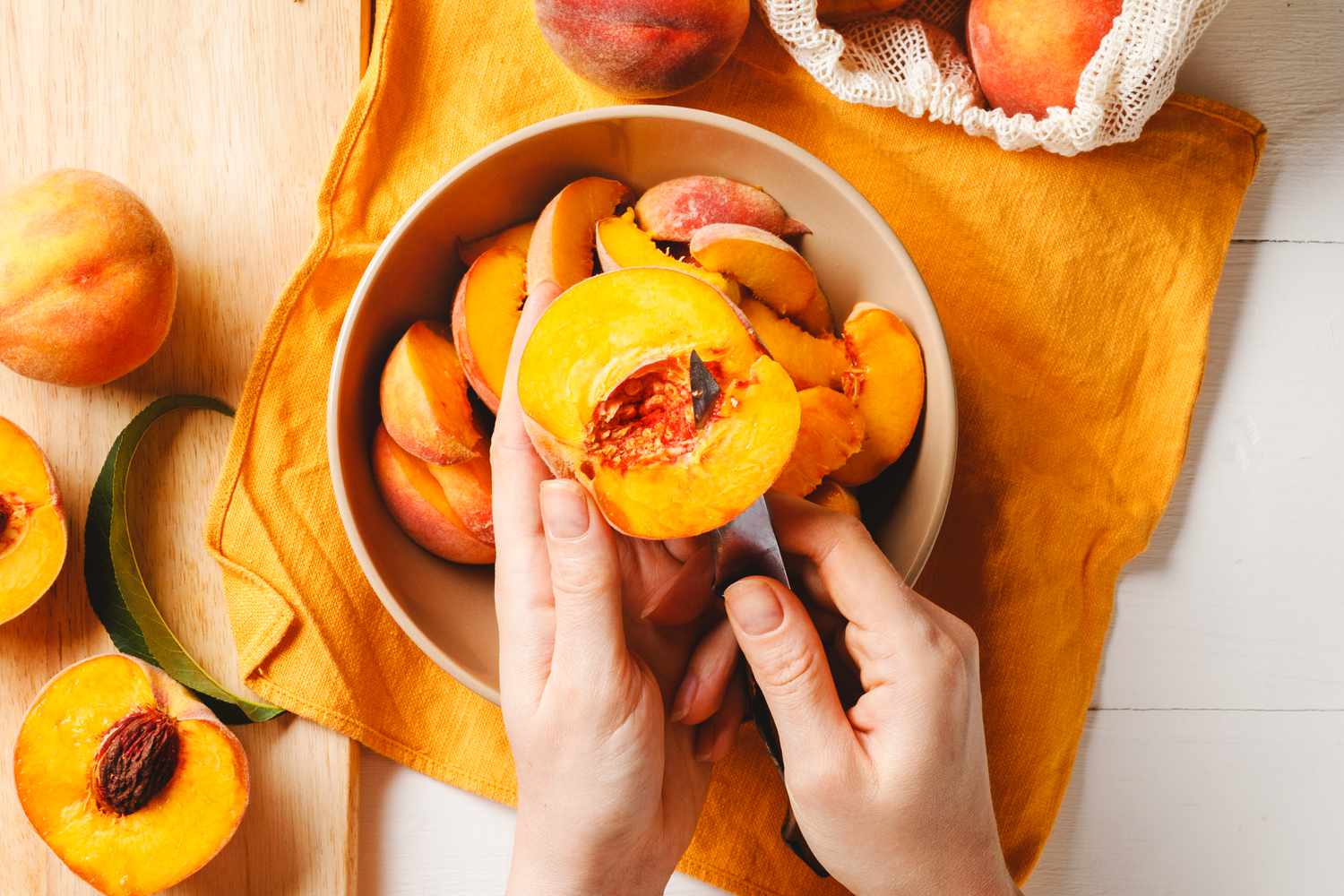 someone cutting fresh peaches into slices over a bowl with peach slices surrounded by more peaches