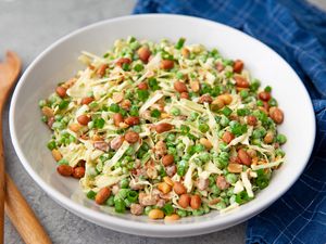 White bowl of cabbage slaw on a gray table with a blue checkered napkin underneath and wooden serving utensils to the side