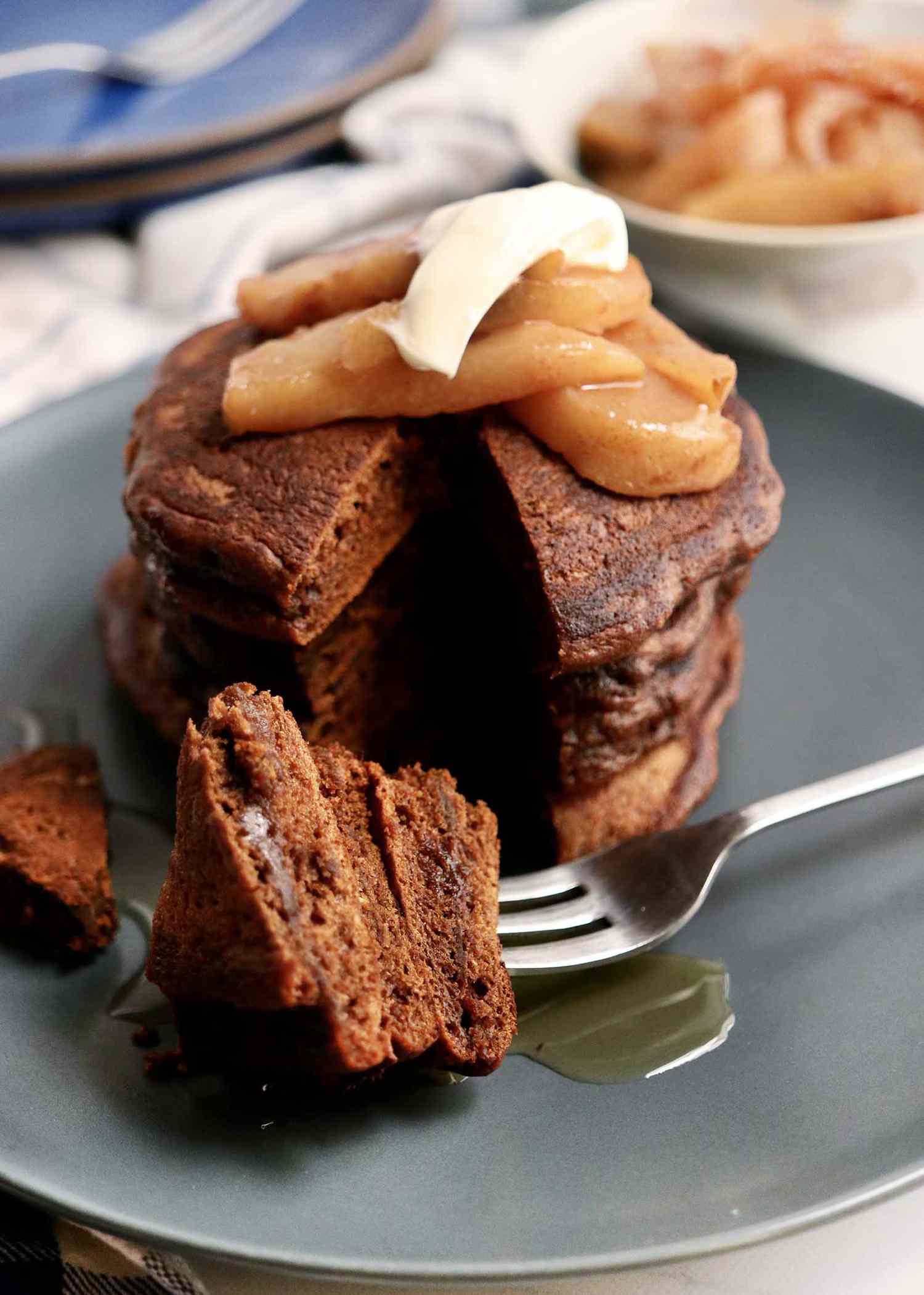 A stack of holiday pancakes with a fork of pancakes set in front of the stack. The pancakes are topped with pears, creme fraiche, and maple syrup.