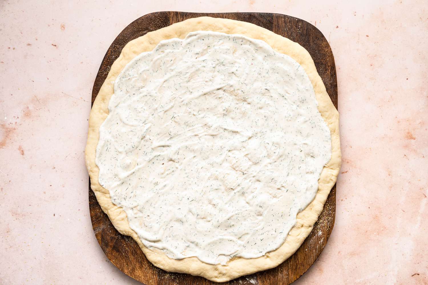 a round of pizza dough with dill sauce for making pickle pizza
