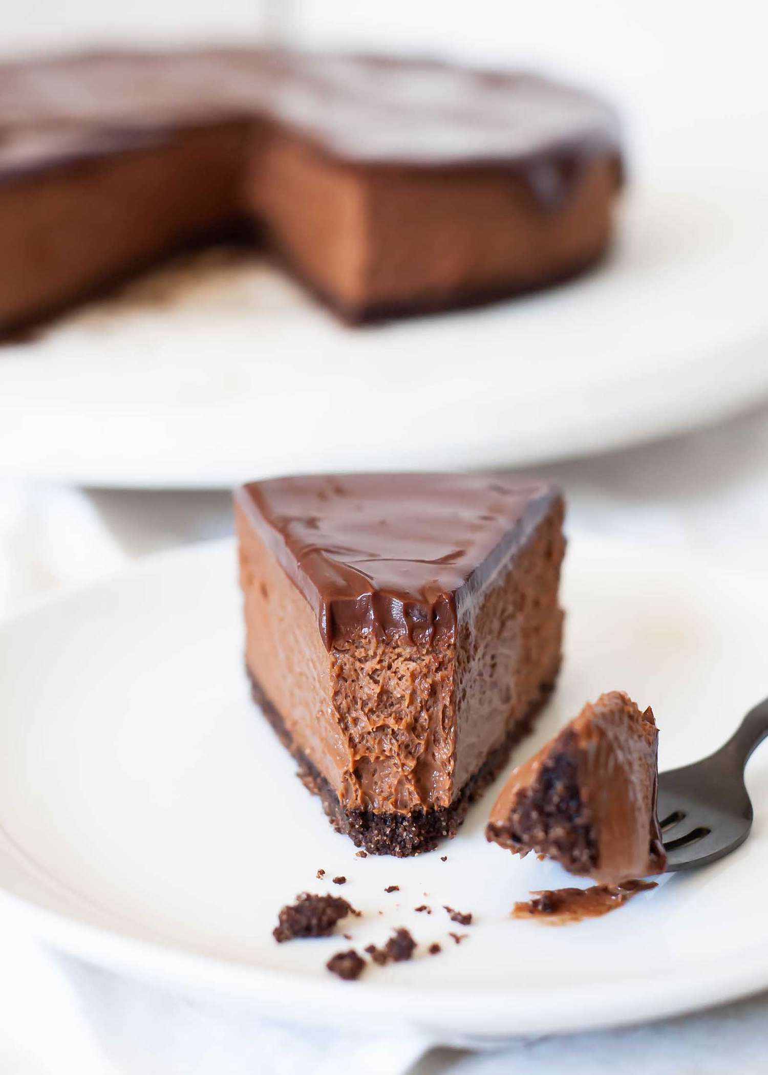 A close up of a slice of chocolate cheesecake with a bite taken out with a fork
