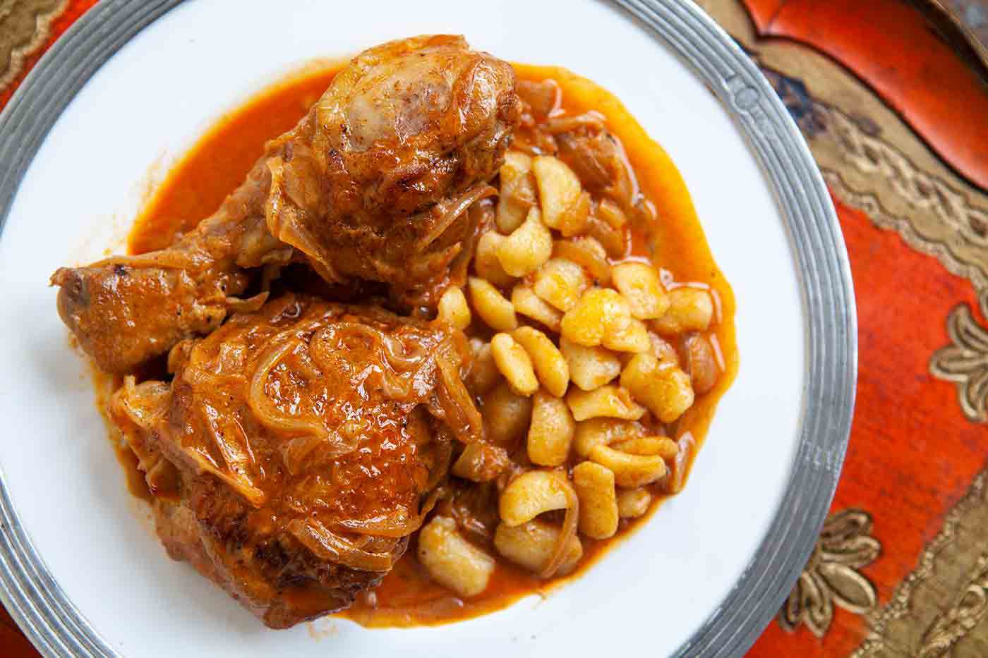 A red tablecloth gives way to a white plate with rich, red chicken paprikash on it