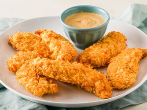Angled view of a white plate of air fryer potato chip chicken tenders along with a small bowl of dipping sauce