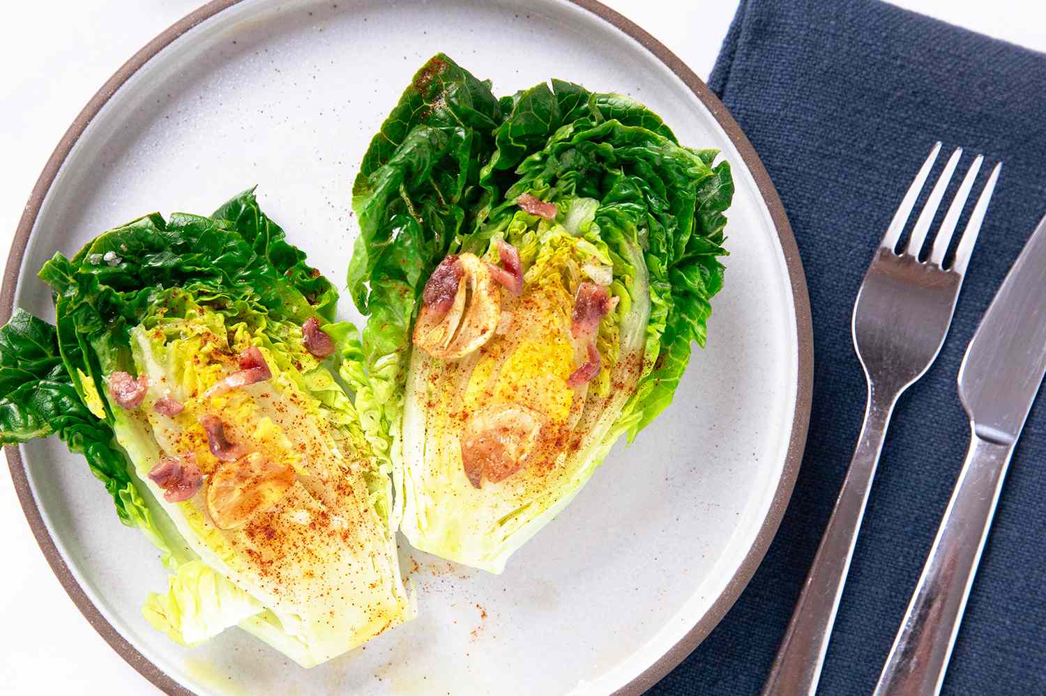 A plate serving two halves of little gem lettuces with a warm garlic dressing and garnishes