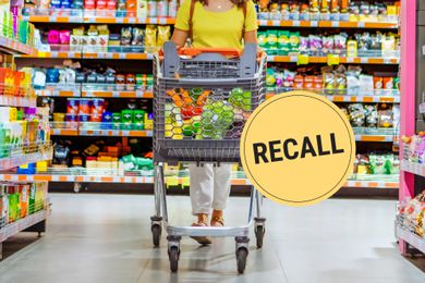 A woman wearing a bright yellow shirt pushing a shopping cart down a grocery store aisle.