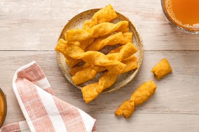 Twisted Cheese Straws on a Plate Next to a Drink and a Kitchen Towel. One Twisted Cheese Straw Is Broken in Half Next to the Plate.
