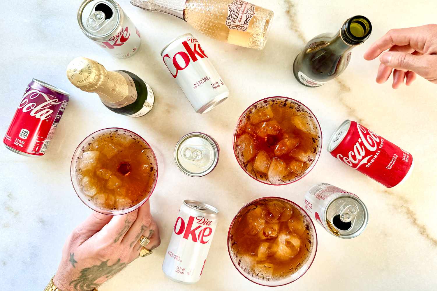 A collection of beverages including Coca-Cola, Diet Coke, and bottles of wine shown with glasses containing a mixed drink