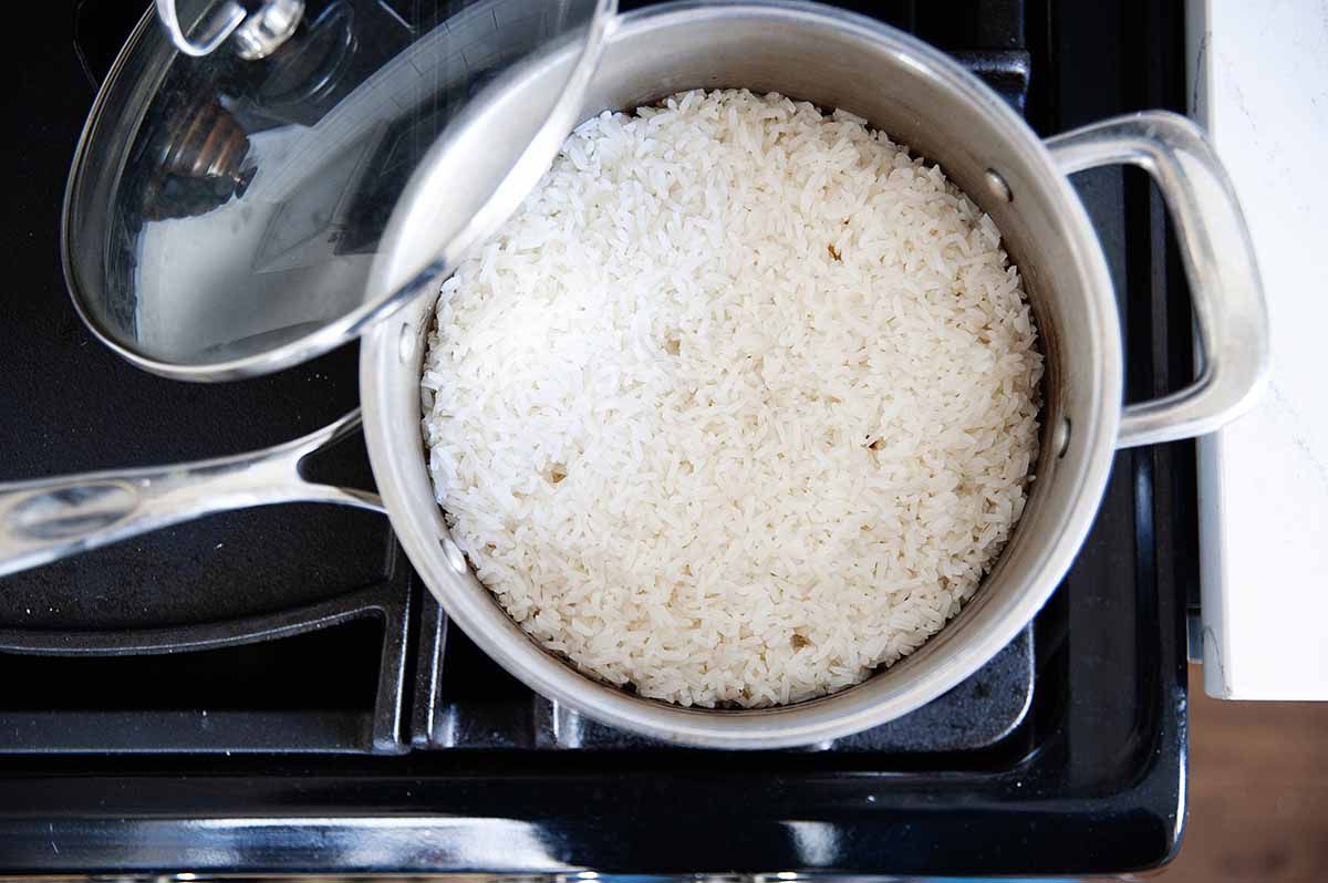 Pot of perfect white rice on a gas stove with the lid resting on the side of the pot.