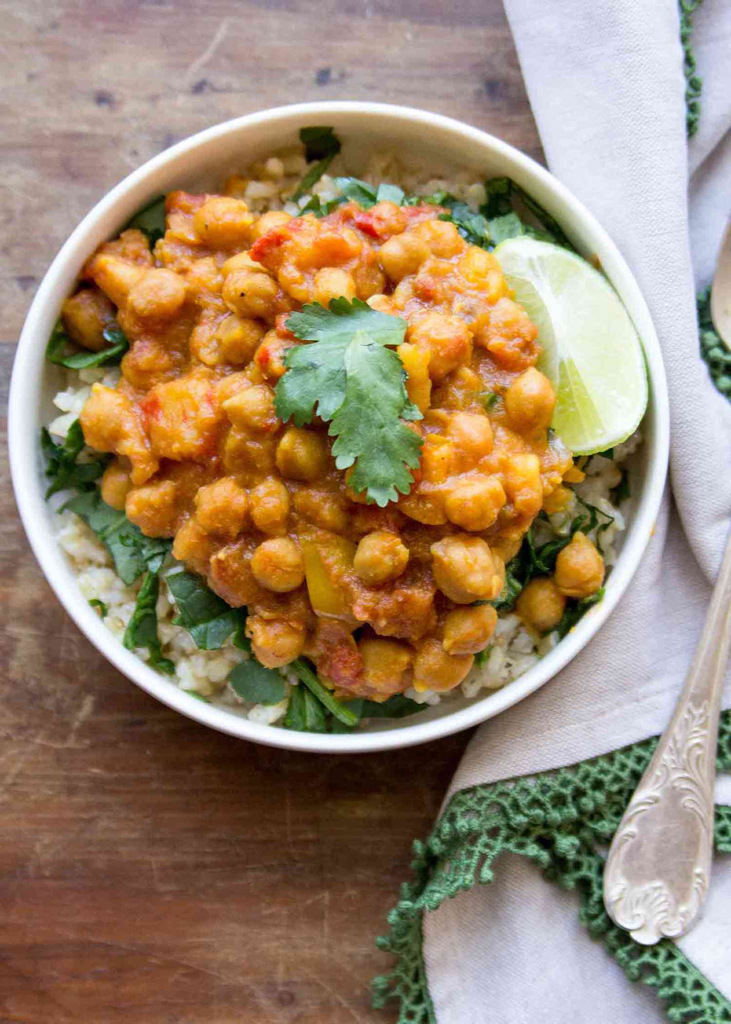 Crockpot Chickpea Curry served in a bowl with fresh spinach, rice, and a wedge of lime.