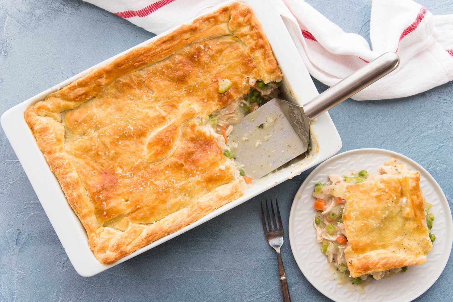 Homemade Chicken Pot Pie with a golden crust has a serving removed and set on a white plate to the right.