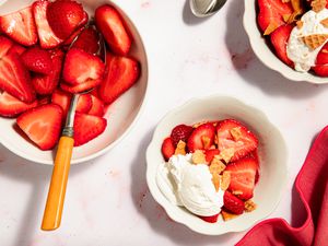 Strawberry dessert bowls with toppings like whipped cream and crushed cookies on a white background