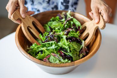 Mixed slad greens getting tossed together in a wooden bowl