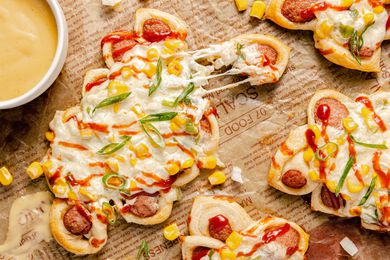 Pull-Apart Corn Cheese Pigs in a Blanket with a Piece Pulled Off, Surrounded by More and a Bowl of Mustard