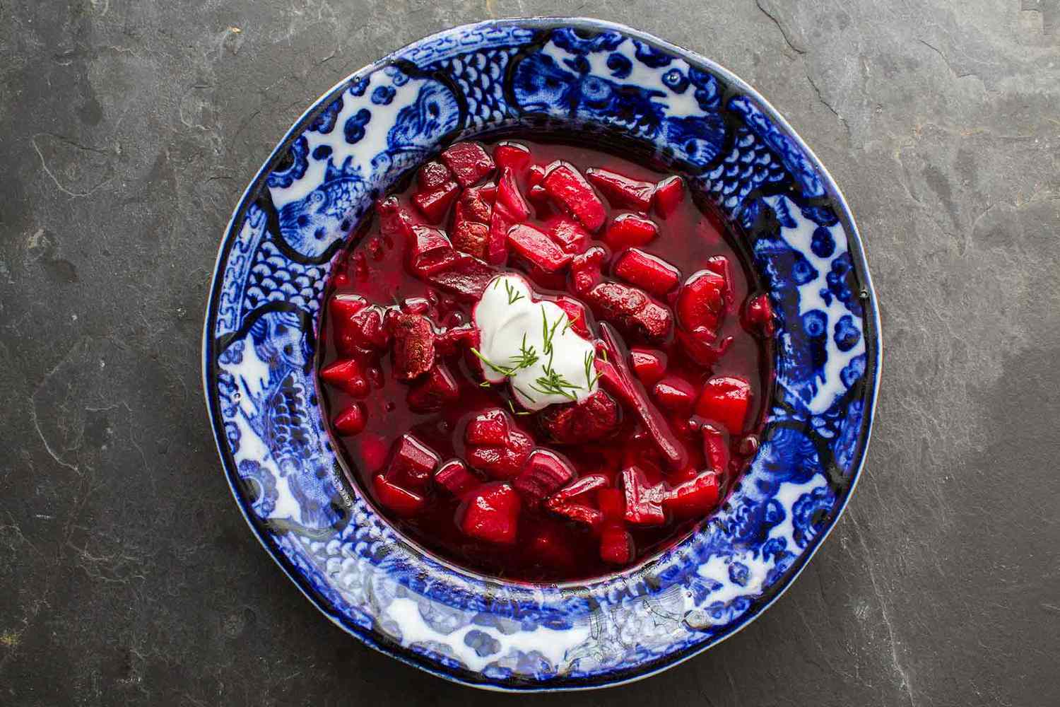 A bowl of beef Borscht with sour cream and dill on top as a garnish