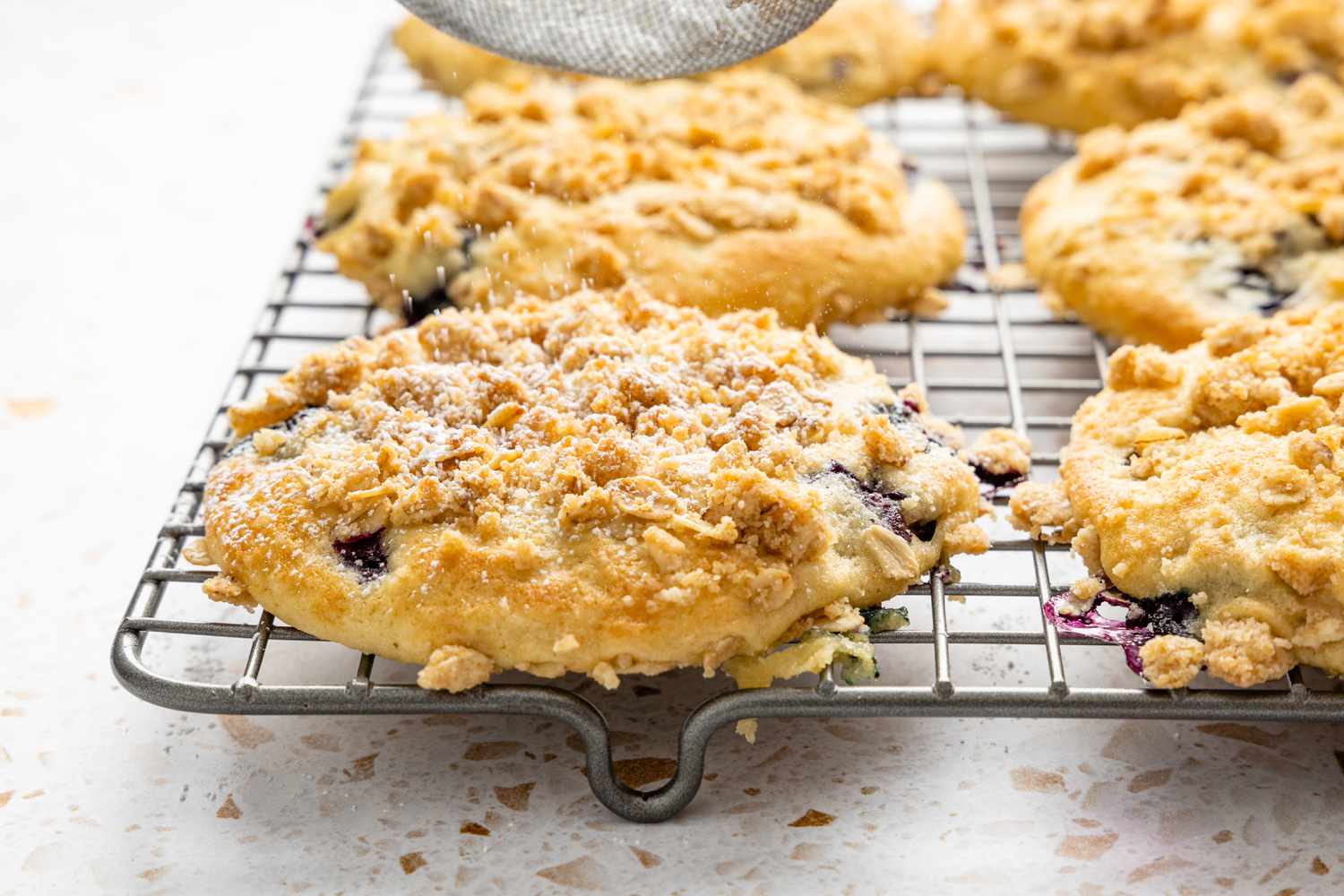 Powdered Sugar Dusted onto Blueberry Muffin Tops Cooling on a Wire Rack