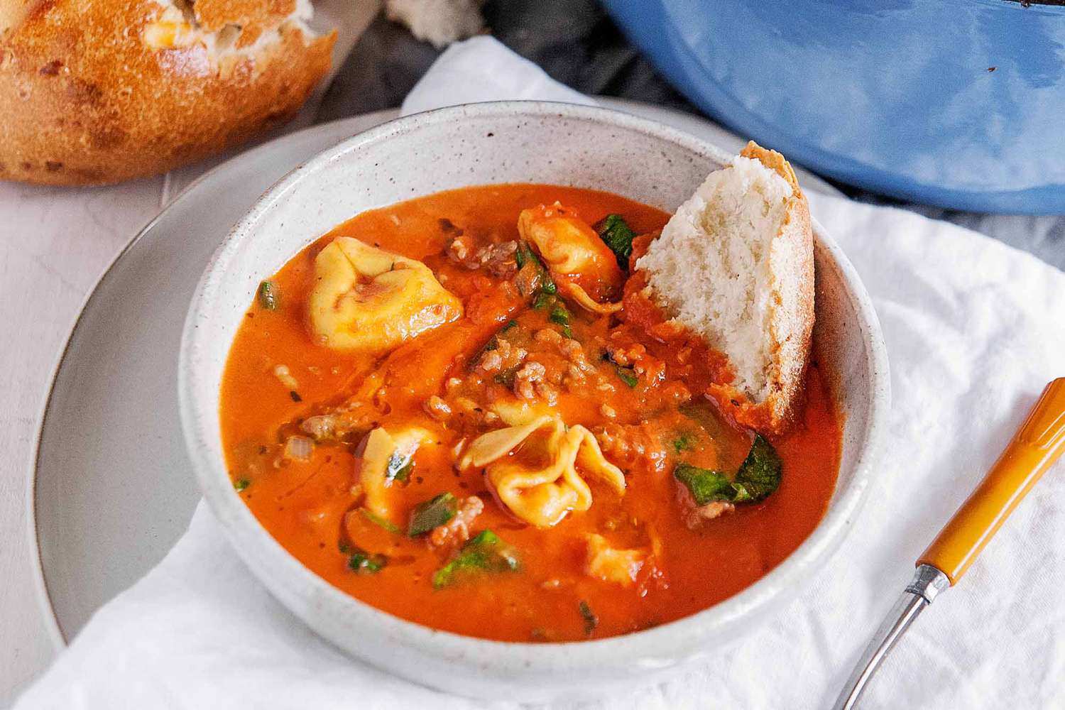 Italian Sausage Tortellini Soup - white bowl with tomato soup, fresh basil and cheese filled tortellini wtih a blue pot in the background