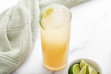 A tall glass of ginger ale soda with a bowl of sliced limes next to it.