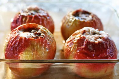 Four baked apples with their tops cut off and resting in a glass baking dish