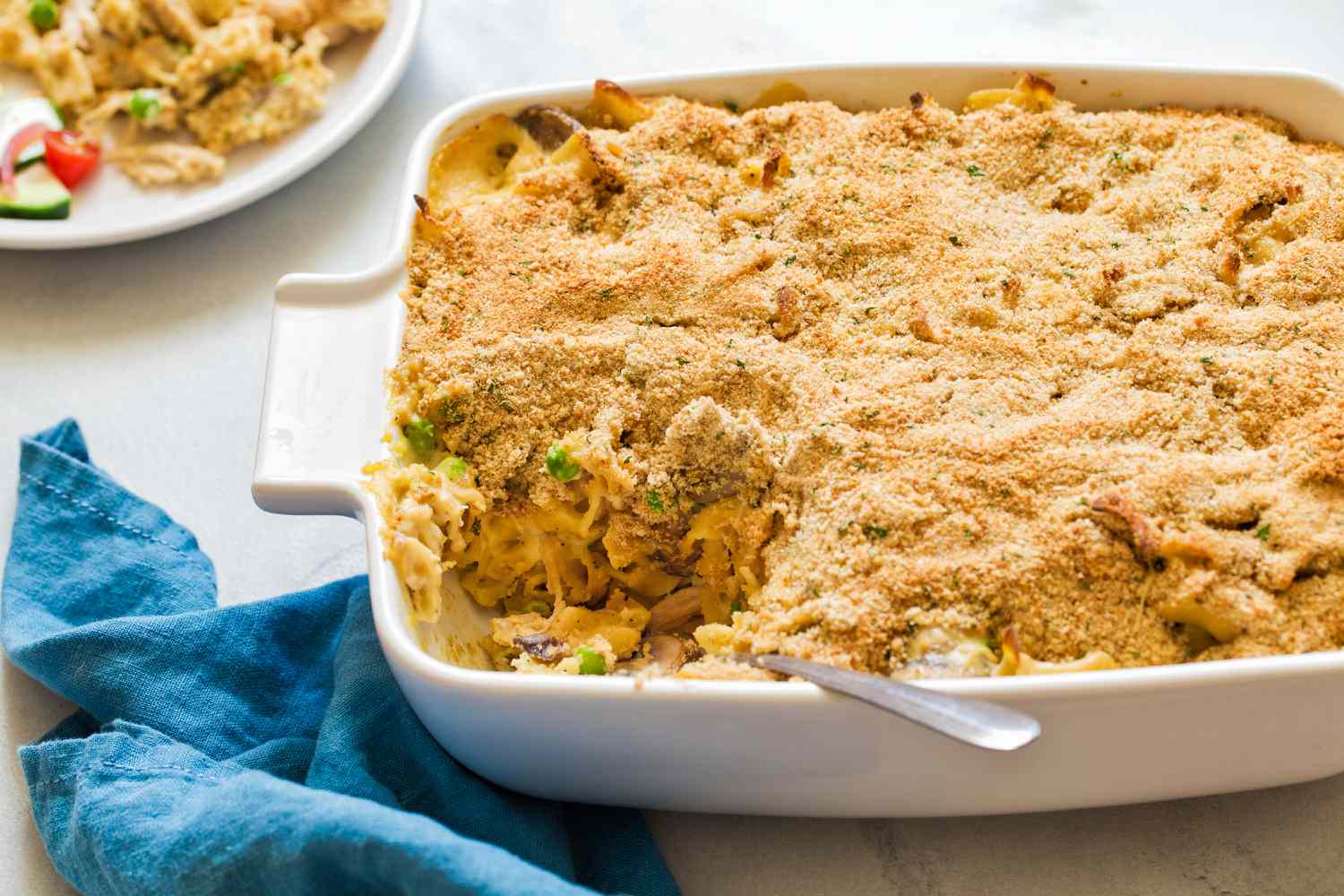Angle view of a white baking dish of chicken tetrazzini with a slice removed next to a blue cloth napkin