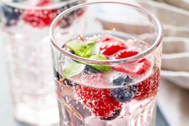 A close-up of a glass of sparkling water with raspberries and blueberries in it
